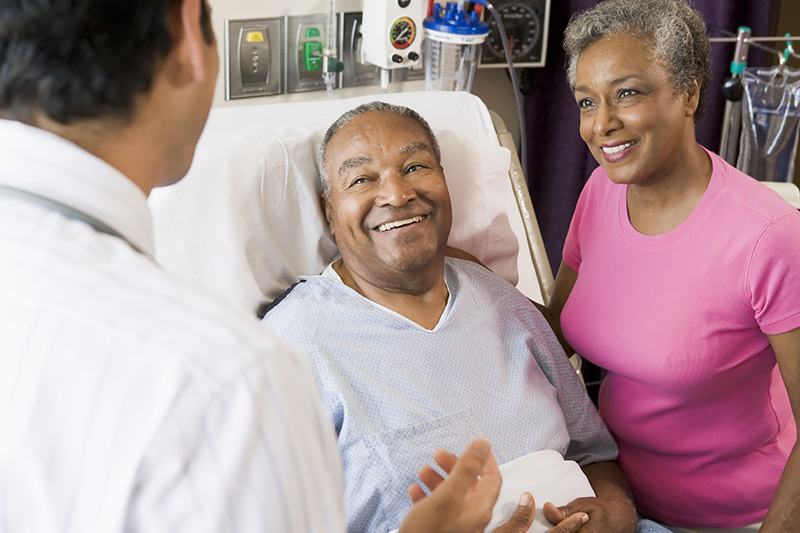 doctor talking with senior man in hospital bed with his wife