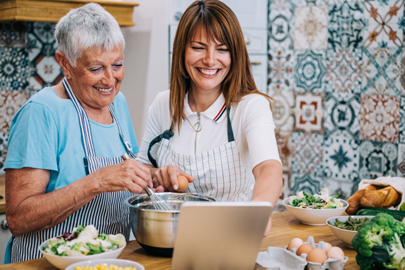 happy senior lady and caregiver cooking